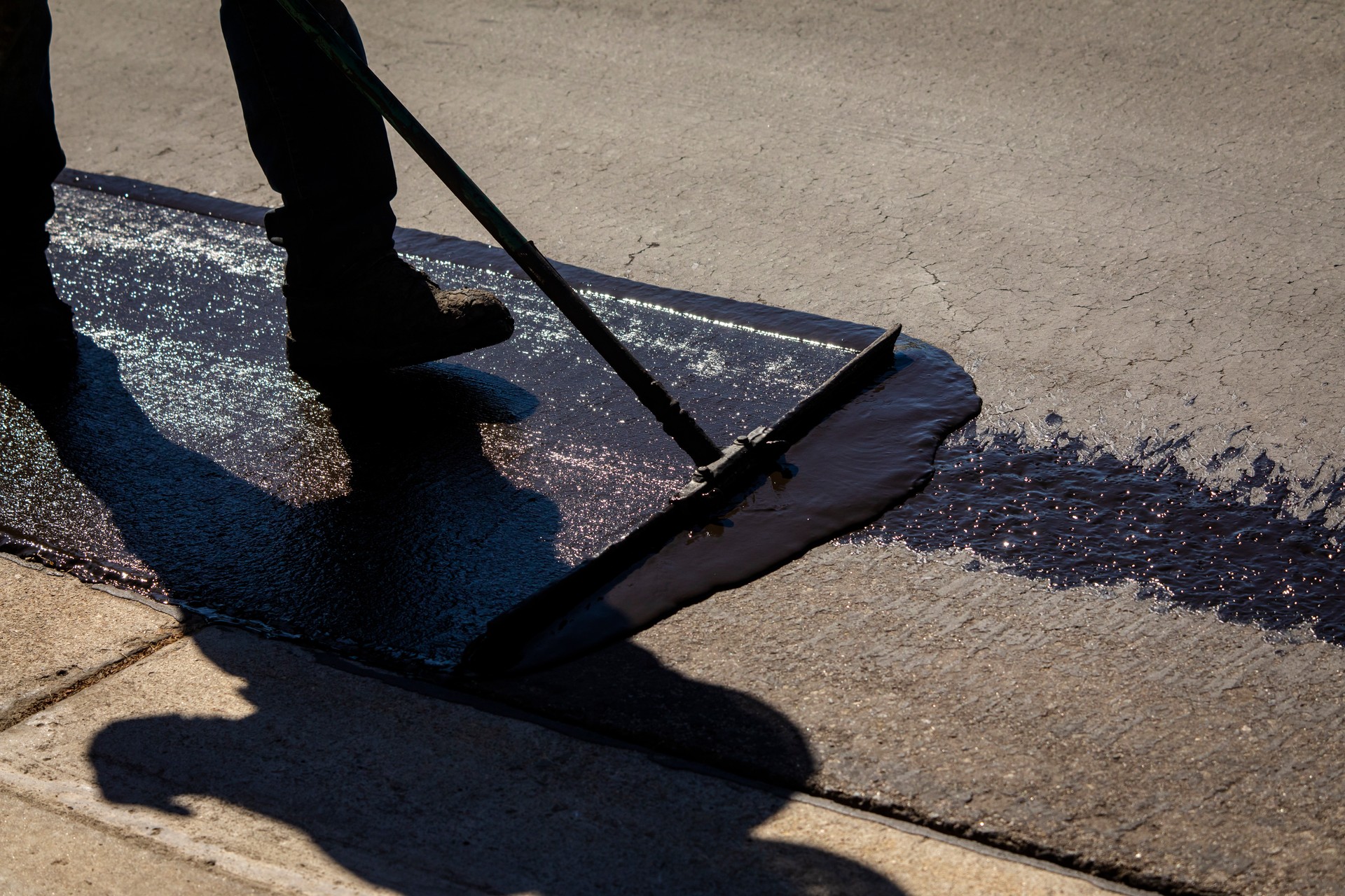 Worker using a sealcoating brush during asphalt resurfacing project